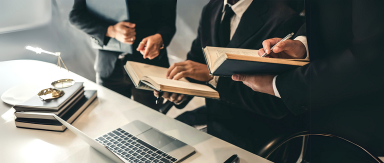 Profissionais consultando livros e documentos ao lado de um notebook
